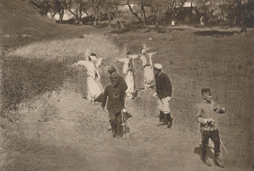 A photo of three Koreans tied to posts and blindfolded. Four soldiers stand nearby.