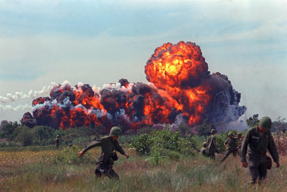A napalm strike erupts in a fireball near U.S. troops on patrol in South Vietnam.jpg