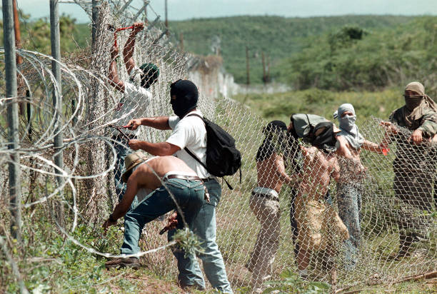 A group of protestors use tools to cut away sections of chain link fence