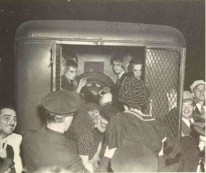 a crowd of people around a police van with folks from the Masque Ball looking out of the back of the police van