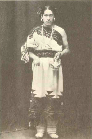 We'Wha, a lhamana wearing the ceremonial regalia of Zuni women standing looking at the camera for a portrait holding a basket