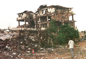 A person stands facing the bombed ruins of a building.